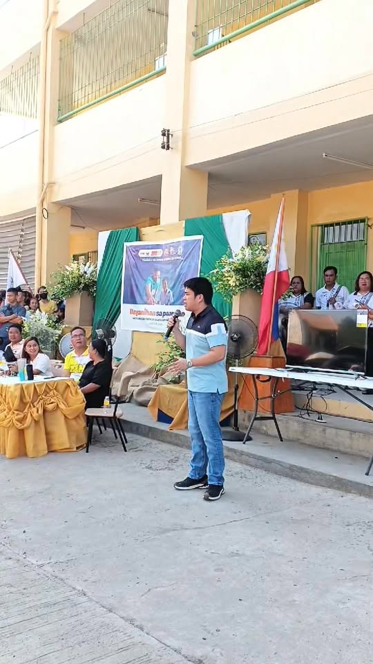 Lalaking nagsasalita sa mikropono sa entablado ng Brigada Eskwela sa Timalan Hillsview Integrated School