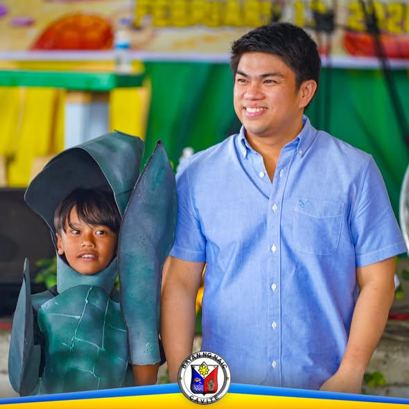 Lalaking nakangiti katabi ng batang naka-kostyum ng pawikan sa Pawikan Festival 2026 sa Naic