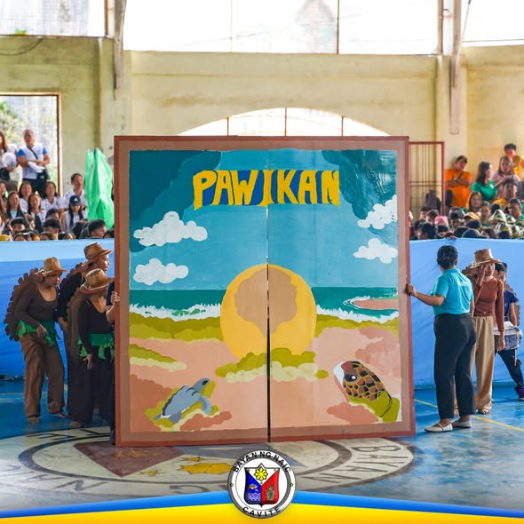 Mga performer na may hawak na backdrop na "PAWIKAN" sa Naic Covered Court habang may Pawikan Festival