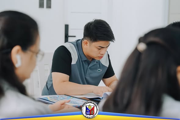Pulong ng Local School Board sa Naic Municipal Hall; isang kalahok na nagbabasa ng mga dokumento sa mesa.