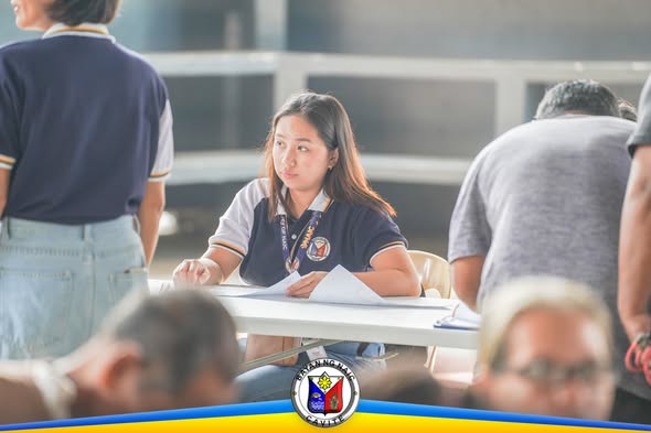 Staff ng Municipal Agriculturist na nakaupo sa mesa habang nagsasagawa ng info-caravan sa Naic Covered Court