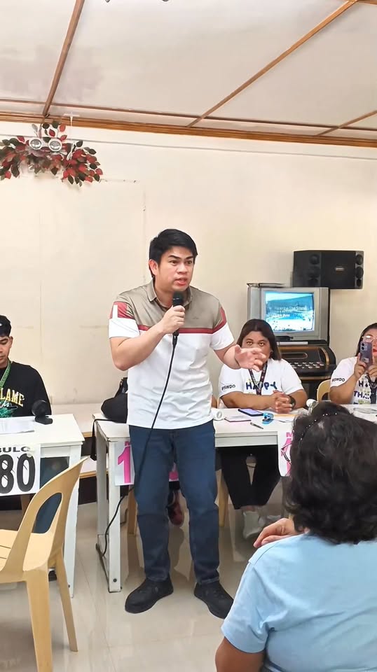 Lalaki na nagsasalita sa mikropono sa harap ng mga nakaupong kalahok ng Localized Social Pension sa Mabulo