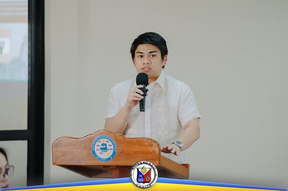 Lalaki na nagsasalita sa mikropono habang nakatayo sa podium sa loob ng pulong sa ABC Hall, Naic