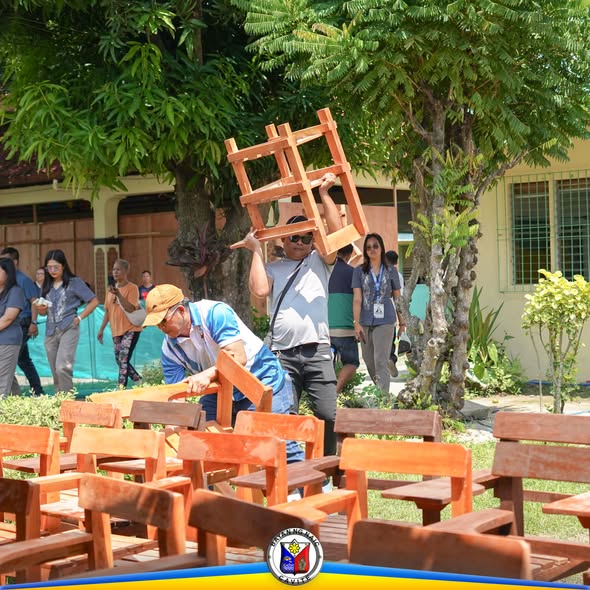 Mga tao habang bumubuhat at nag-aayos ng mga wooden school chairs sa labas ng paaralan