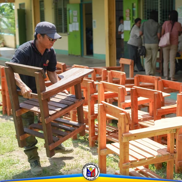 Lalaking nagbubuhat ng bagong gawang kahoy na school chair sa labas ng paaralan sa Naic