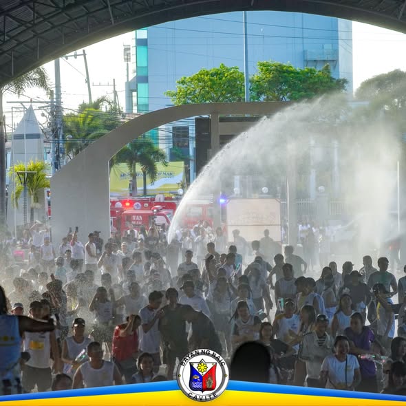 Maraming tao sa ilalim ng arko habang tinatamaan ng tubig mula sa fire truck sa Naic Town Plaza