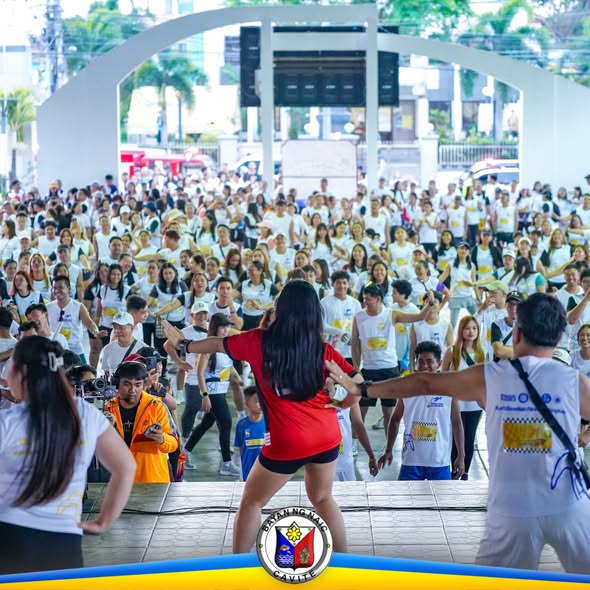 Mga kalahok na naka-puting damit habang sumasayaw ng zumba sa Naic Town Plaza kasama ang instructor sa entablado