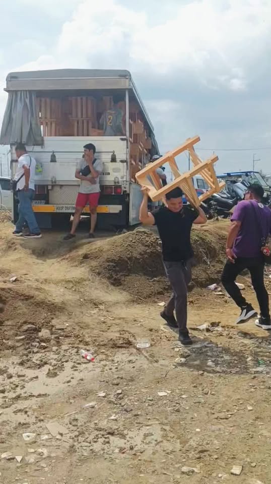 Lalaking nagbubuhat ng upuang kahoy sa lupang daan habang ibinababa ang mga upuan mula sa trak sa Timalan Hillsview