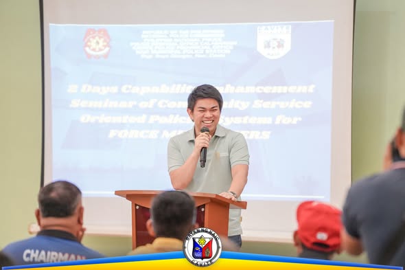 Nagsasalita ang isang lalaki sa mikropono sa harap ng podium habang nakikinig ang mga dumalo sa seminar ng Force Multipliers