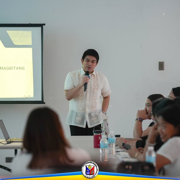 Nagsasalita sa mikropono ang isang lalaki sa harap ng screen sa Triple 8 Hall, Barangay Sabang, Naic