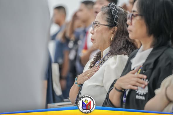 Mga kalahok na nakatayo at nakahawak sa dibdib habang isinasagawa ang flag raising ceremony sa Naic