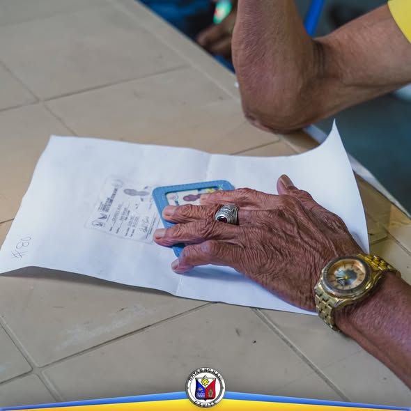 Kamay ng matandang benepisyaryo habang hawak ang ID sa pamamahagi ng Social Pension sa Villa Apolonia