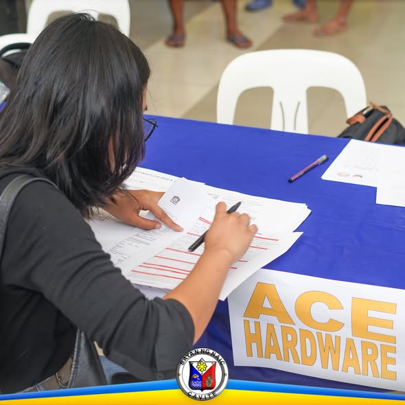 Babaeng nagsasagot ng form sa mesa para sa Job Fair sa Naic, may banner ng ACE Hardware