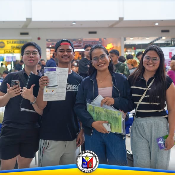 Mga kabataan na nakangiti habang may hawak na papel at folder sa Job Fair 2026 sa Naic