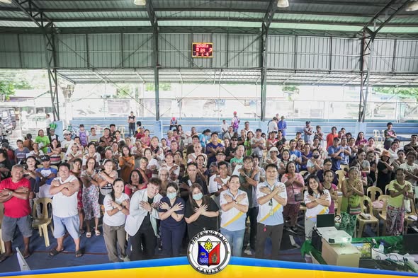 Mga tao sa covered court habang nakatayo at nakakrus ang mga braso sa PhilHealth YAKAP para sa Manggagawa sa Timalan…