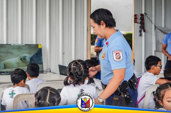 Pulis na kasama ang mga batang nakaupo sa covered court habang isinasagawa ang Kabataan Kontra Droga at Terorismo