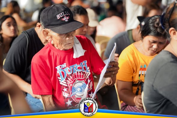Matandang lalaki na nagbabasa ng papel habang naghihintay sa payout ng UPLIFT sa Naic Town Plaza