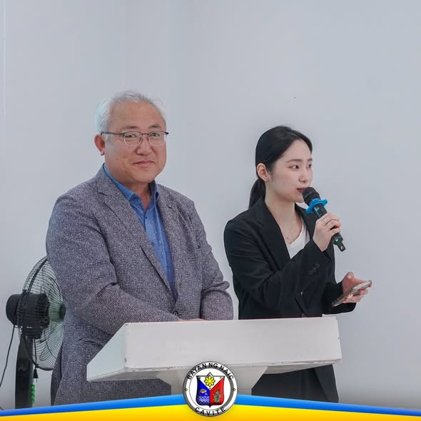 Dalawang tao sa likod ng podium habang nagsasalita ang babae sa mikropono sa MOU signing ng Naic