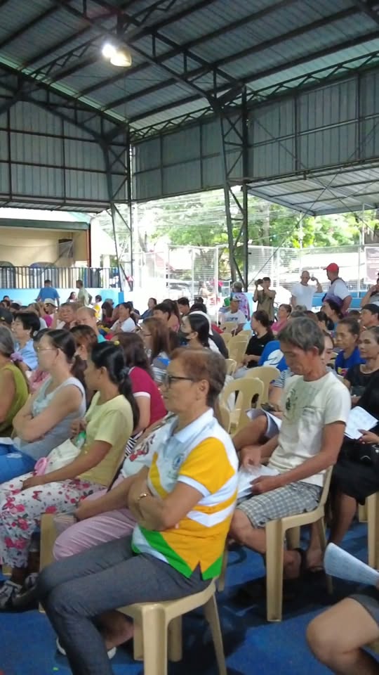Mga residente na nakaupo sa covered court habang nagaganap ang PhilHealth Yakap Program sa Timalan Concepcion