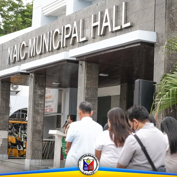Mga tao sa harap ng Naic Municipal Hall habang may nagsasalita sa podium sa flag raising ceremony