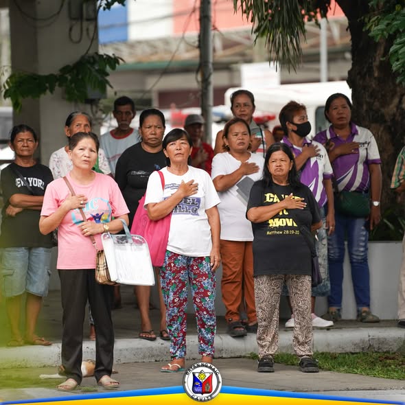 Mga tao na nakatayo at nakahawak sa dibdib habang nagaganap ang flag raising ceremony sa Naic Municipal Hall