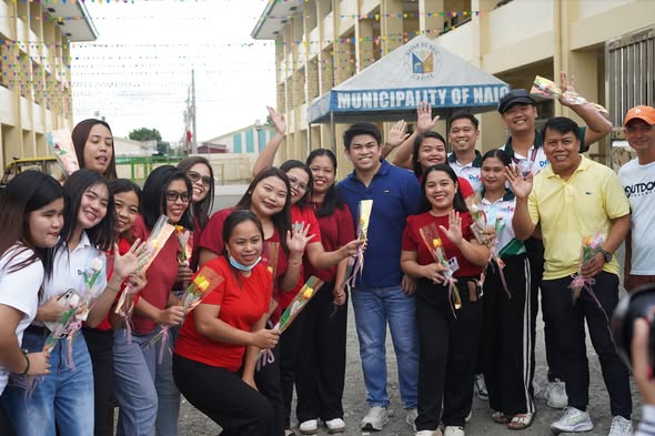 Mga tao na may hawak na bulaklak at kumakaway sa harap ng Municipality of Naic para sa Araw ng mga Puso