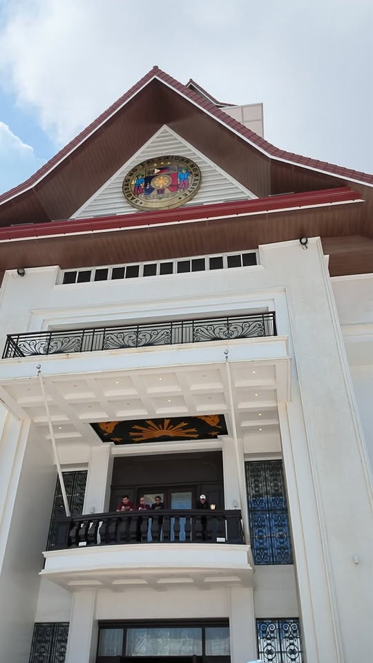 Harapan ng New Provincial Government Center na may emblem at balkonaheng may ilang tao, Trece Martires City