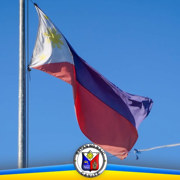 Watawat ng Pilipinas na nagwawagayway sa poste laban sa asul na langit, may selyo ng Bayan ng Naic
