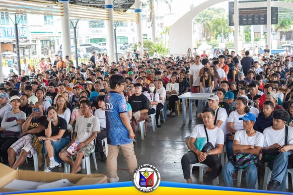 Maraming tao na nakaupo sa covered court habang nagsasalita ang isang opisyal ng LTO sa Naic Town Plaza