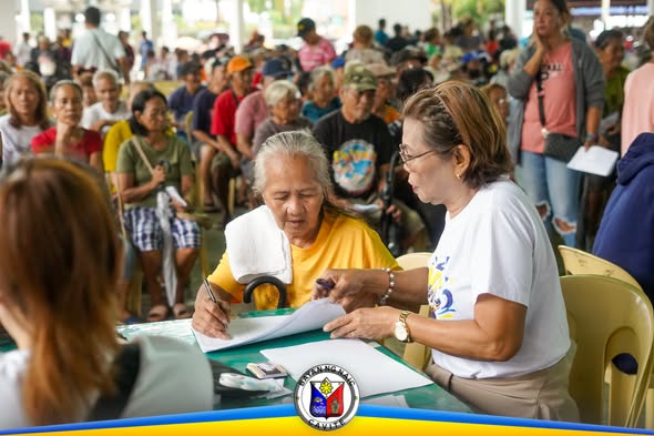 Mga senior citizen na pumipirma ng dokumento habang inaasikaso ng staff sa National Social Pension sa Naic Town Plaza