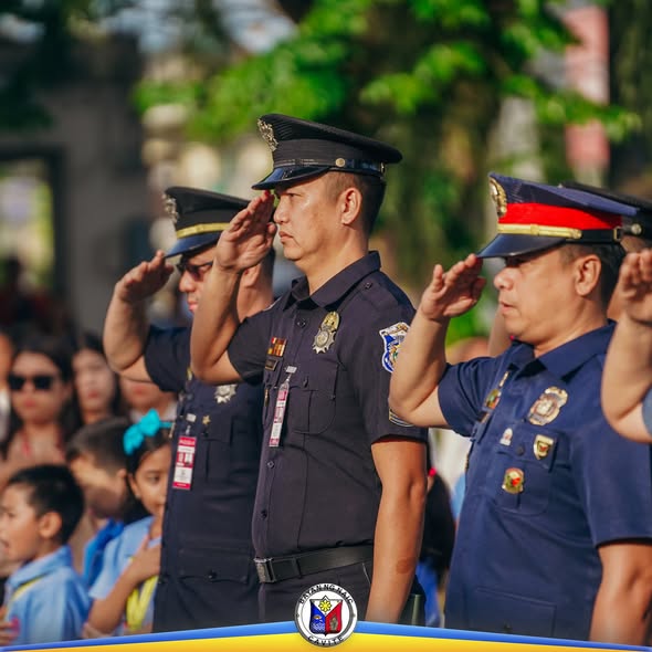 Mga pulis na nagsasaludo sa flag raising ceremony sa Naic Municipal Hall, may mga batang estudyante sa likuran