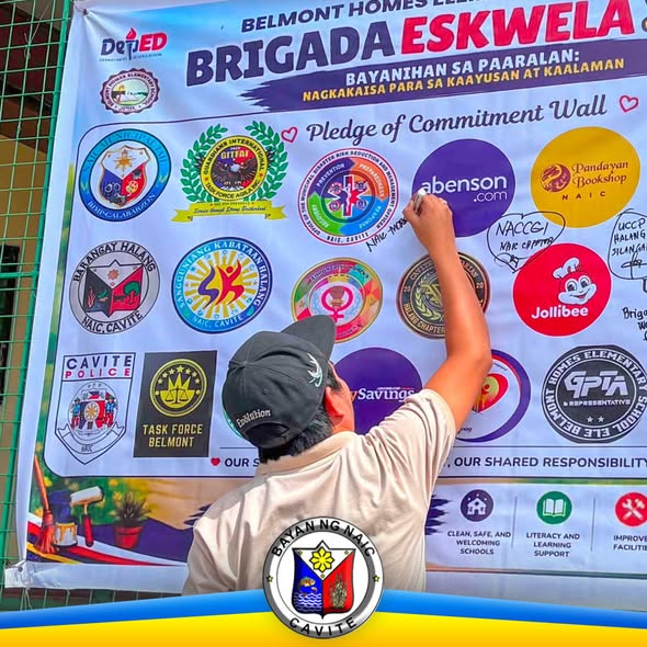 Lalaki habang nagsusulat sa Pledge of Commitment Wall ng Brigada Eskwela sa Belmont Homes Elementary School