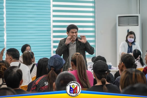 Lalaking nagsasalita sa harap ng mga tao sa loob ng hall sa Brgy. Sabang, Naic, may libreng pustiso na programa