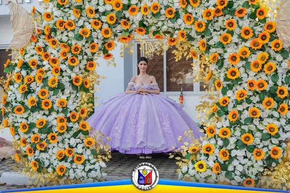 Isang babae sa lavender na gown habang nakatayo sa arko ng puting rosas at sunflower sa SAGAYLA 2026
