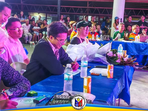 Lalaking nagsusulat sa mesa habang nanonood ang mga tao sa SAGAYLA 2026 sa Naic Town Plaza