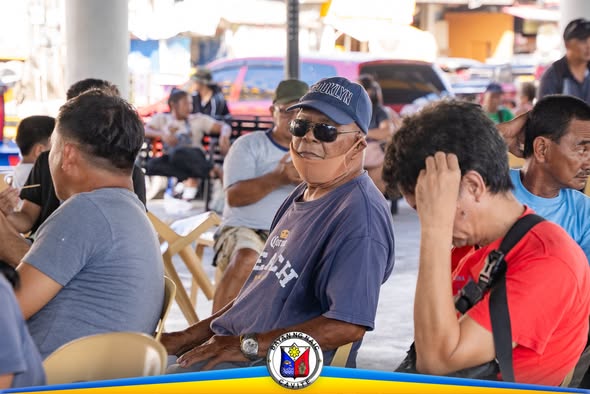Mga magsasakang nakaupo habang naghihintay sa pamamahagi ng binhi sa Naic Town Plaza