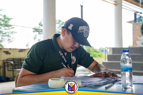 Lalaki na nagsusulat ng mga dokumento sa mesa habang nagdi-distribute ng binhi sa Naic Town Plaza