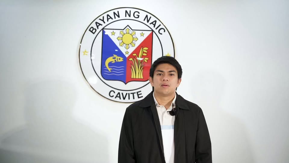 Lalaking nagsasalita sa harap ng logo ng Bayan ng Naic, Cavite, para sa anunsyo ng MR SIA laban sa tigdas
