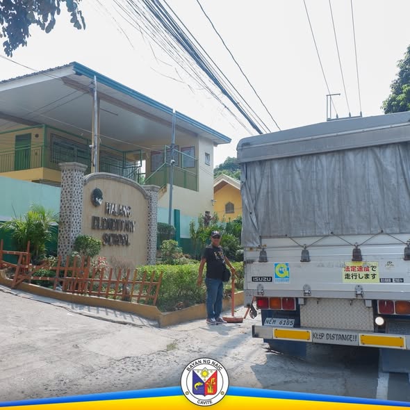Litrato: Lalaking nakatayo sa tabi ng trak sa harap ng Halang Elementary School habang may ipinamamahaging supplies