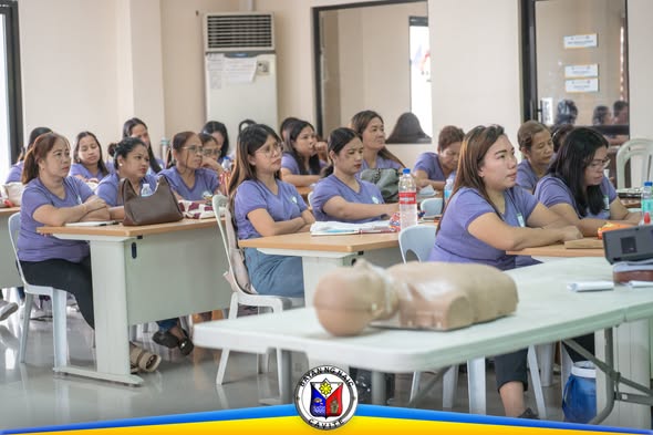 Mga day care teacher na nakaupo sa BLS training sa Liga ng mga Barangay Building, may CPR manikin sa harap