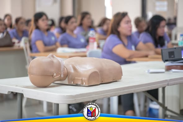 Mga Day Care Teacher na nakaupo habang nagsasanay ng BLS gamit ang CPR manikin sa Liga ng mga Barangay Building