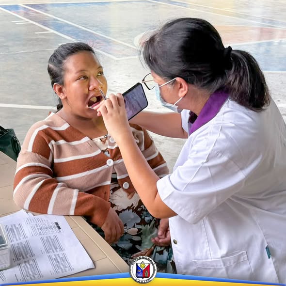 Tauhan ng MHO na sinusuri ang bibig ng isang babae sa covered court habang isinasagawa ang oral health checkup