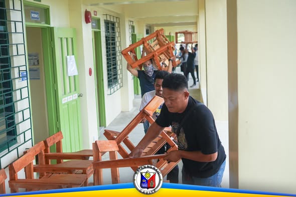 Mga kalalakihang nagdadala ng mga upuan sa paaralan sa corridor ng Timalan Hills View Integrated School