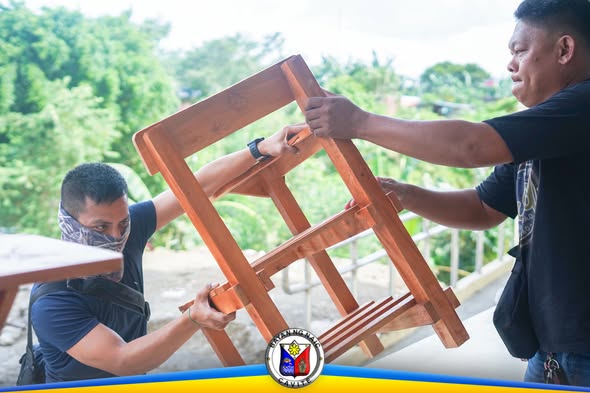 Mga kawani habang binubuhat ang bagong kahoy na school chair sa labas ng paaralan