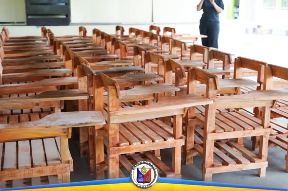 Mga bagong wooden school chairs na nakahanay sa loob ng covered area para sa pamamahagi sa mga paaralan