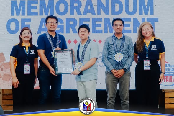 Pirma ng Memorandum of Agreement ng Naic at DMW; limang tao ang nakatayo sa entablado at may hawak na sertipiko