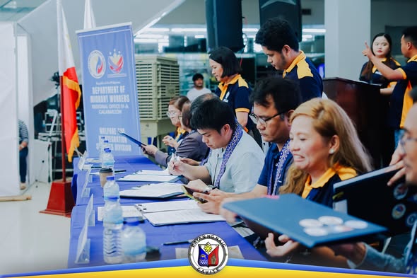 Mga kawani ng DMW na nagproseso ng dokumento sa registration desk sa Stadium Shopping Strip, Naic