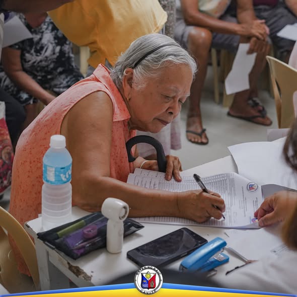 Matandang babae habang nagsusulat sa form ng Localized Social Pension sa Barangay Mabolo, Naic