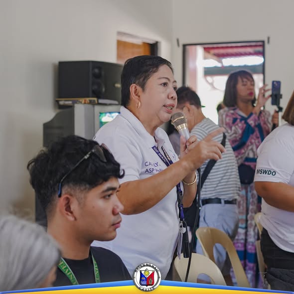 Babaeng opisyal na nagsasalita sa mikropono habang may ginaganap na Localized Social Pension sa barangay
