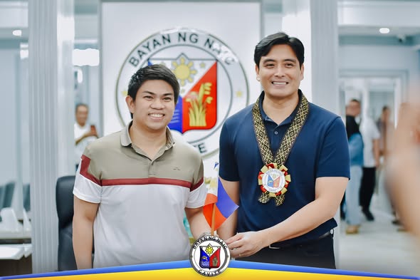 Dalawang lalaking nakangiti sa opisina ng Bayan ng Naic, may seal ng bayan sa likod